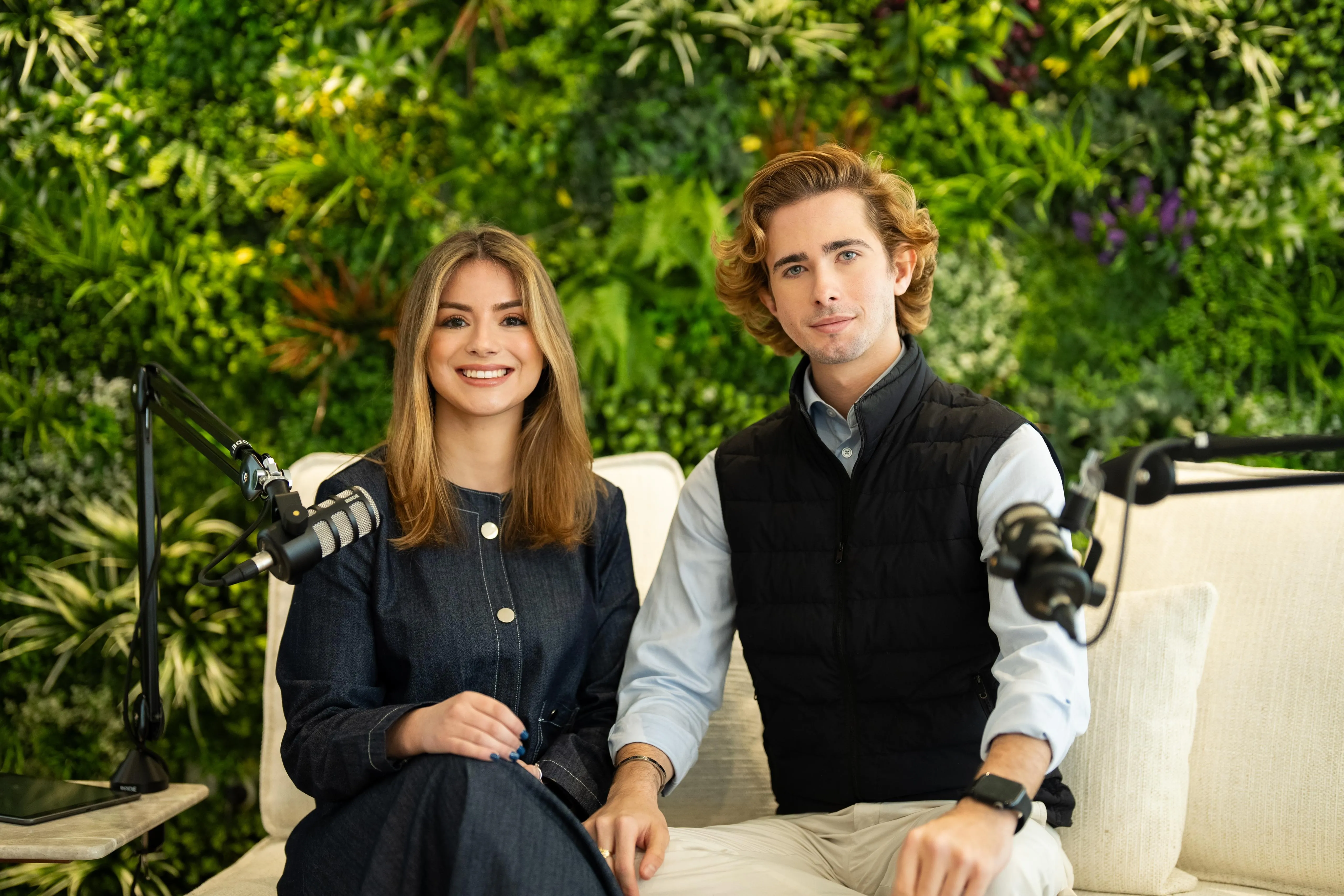 Two hosts in conversation in a studio with a living wall backdrop